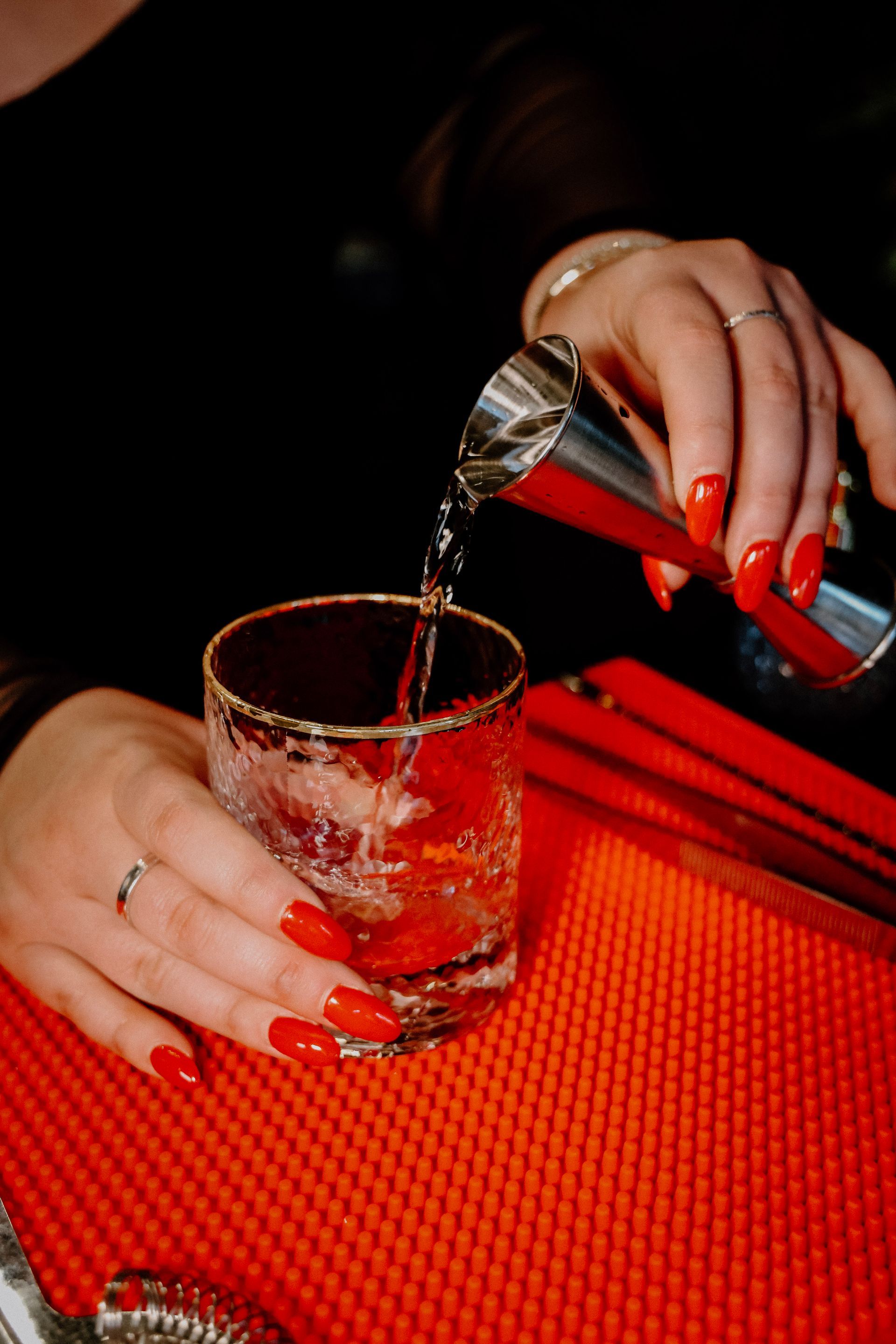 A woman with red nails is pouring a drink into a glass.