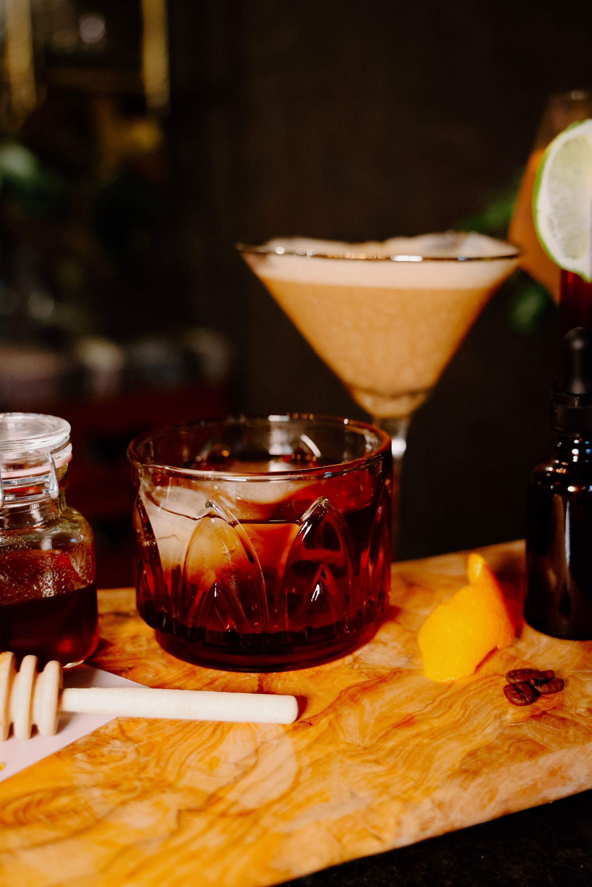 A wooden cutting board topped with a glass of whiskey and a martini.
