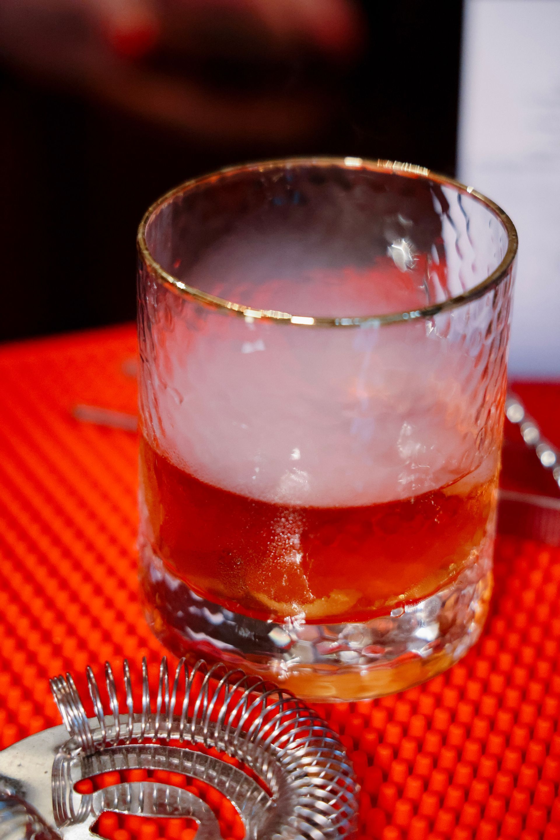 A glass of whiskey with smoke coming out of it is on a red table.