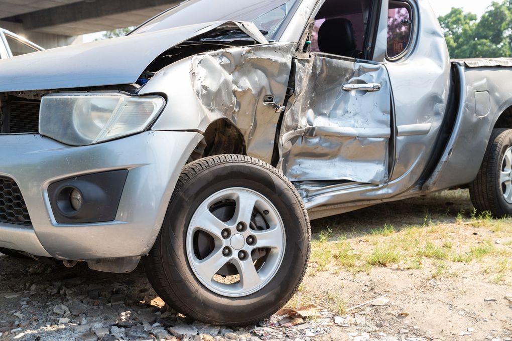 A pickup truck that has been damaged in an accident is parked in the dirt.