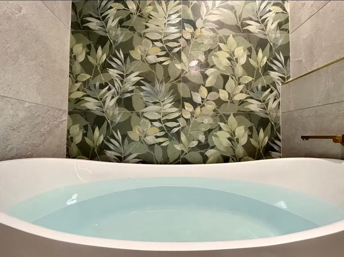 A bathtub filled with blue water in a bathroom with a floral wallpaper on the wall.