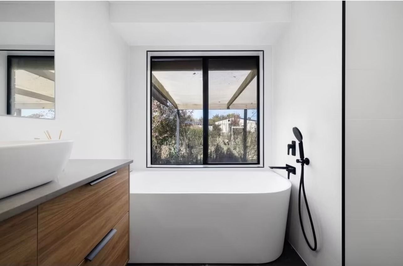 A bathroom with a tub , sink , mirror and window.