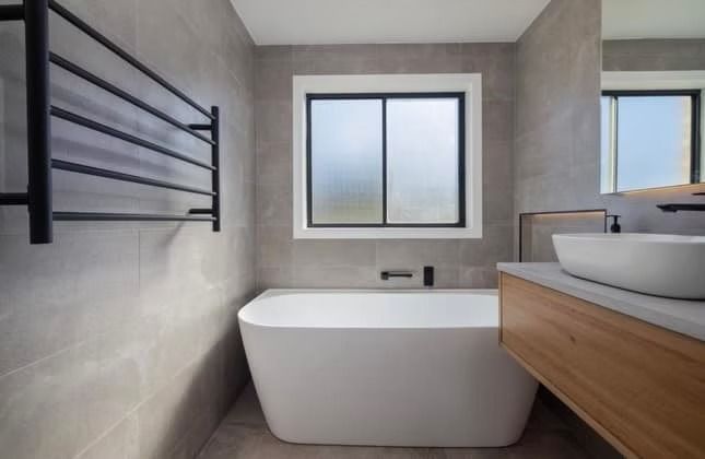 A bathroom with a bathtub , sink , mirror and window.