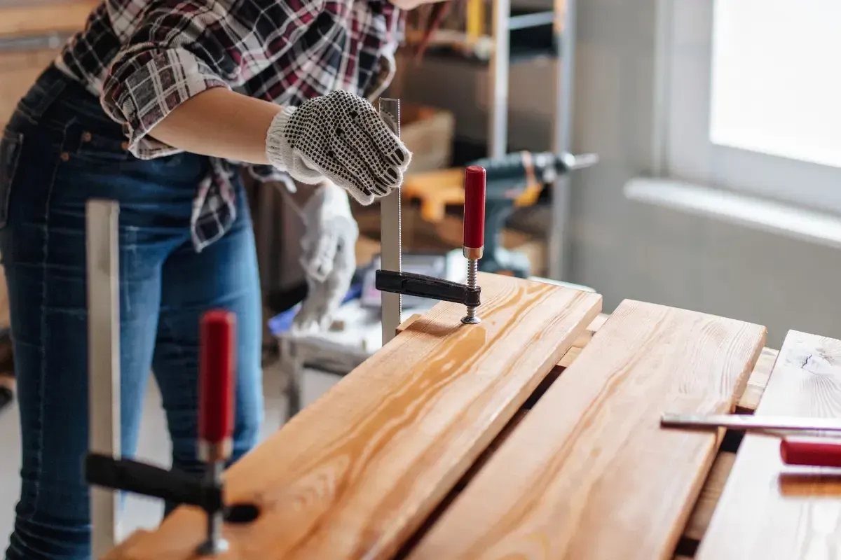 Woman wearing gloves gluing and clamping wood boards in a workshop.