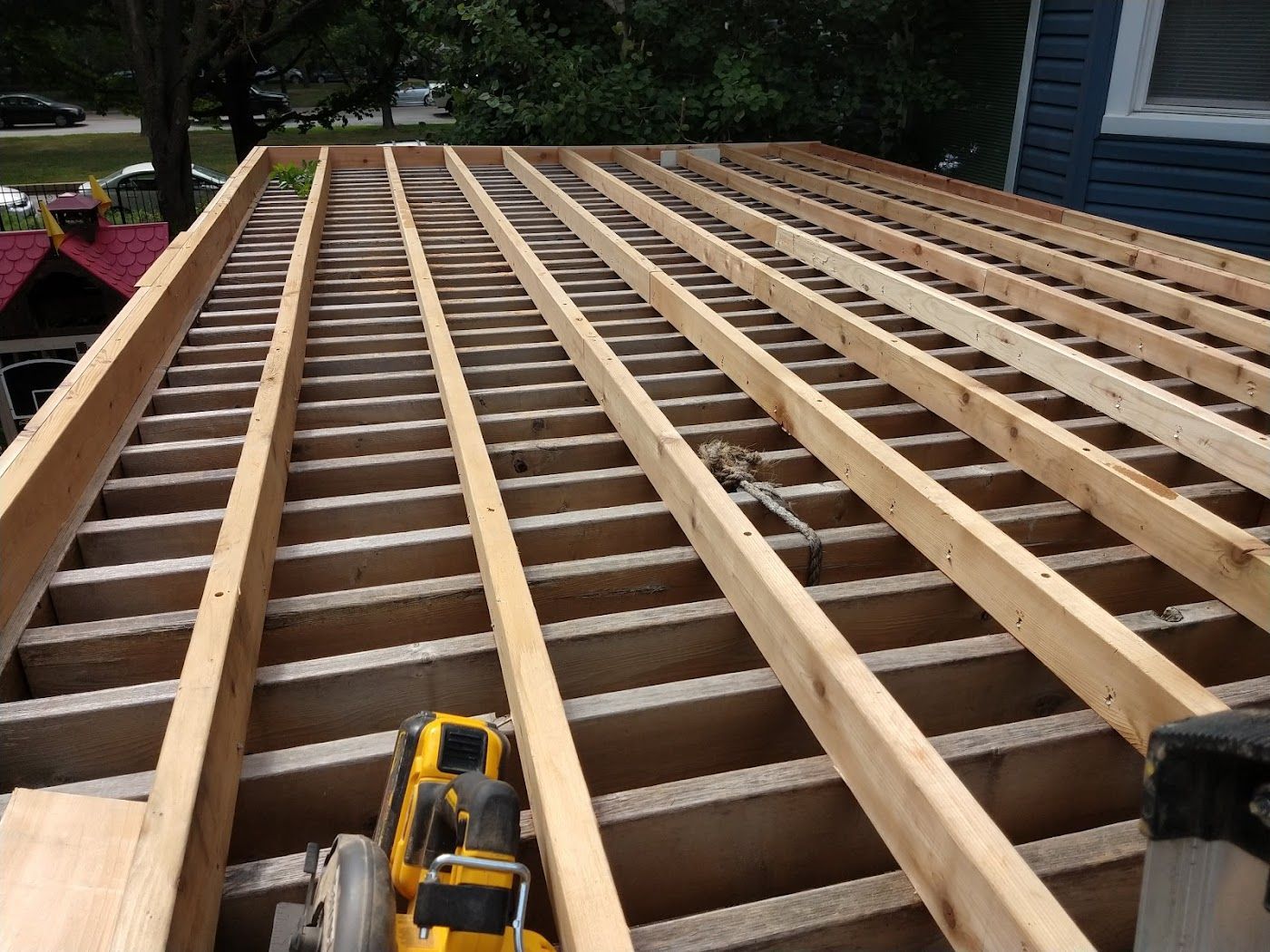 Wooden roof framework under construction, viewed from above. Boards are laid across supporting beams.