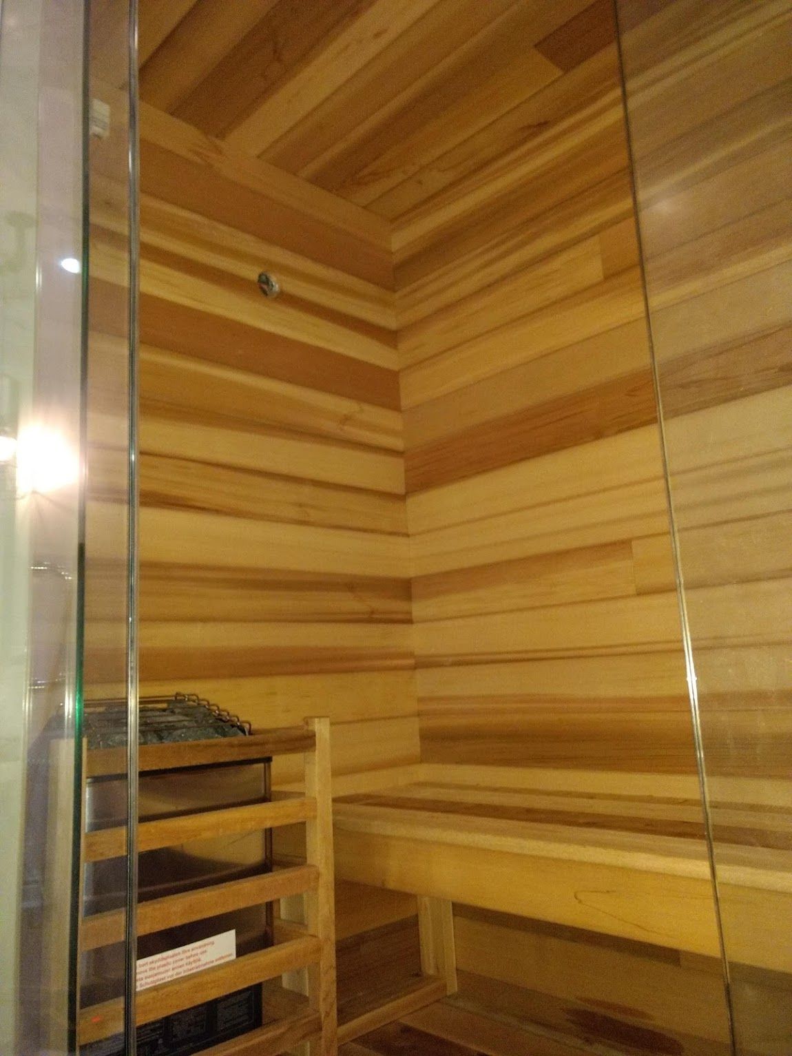 Wooden sauna interior with horizontal wood paneling and bench; glass door on right.