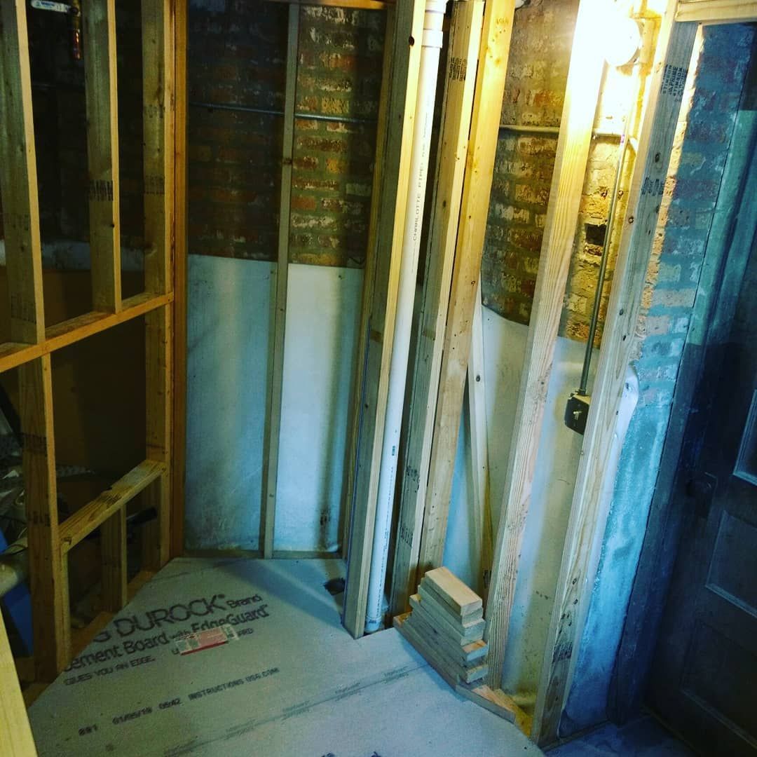 Bathroom under construction with exposed framing, concrete board floor, and plumbing.