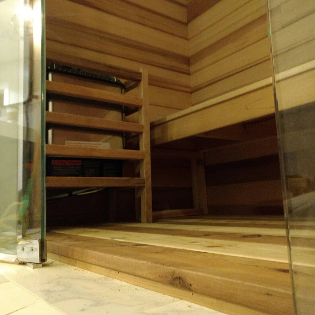 Interior of a wooden sauna. Bench, shelves, and stairs are visible. Glass door on the right.