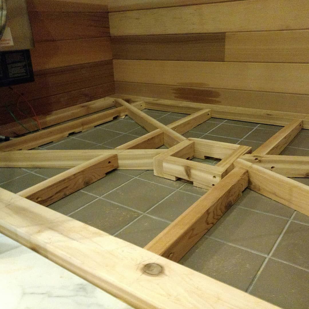Wooden frame construction on tiled floor, inside a room with wood-paneled walls.