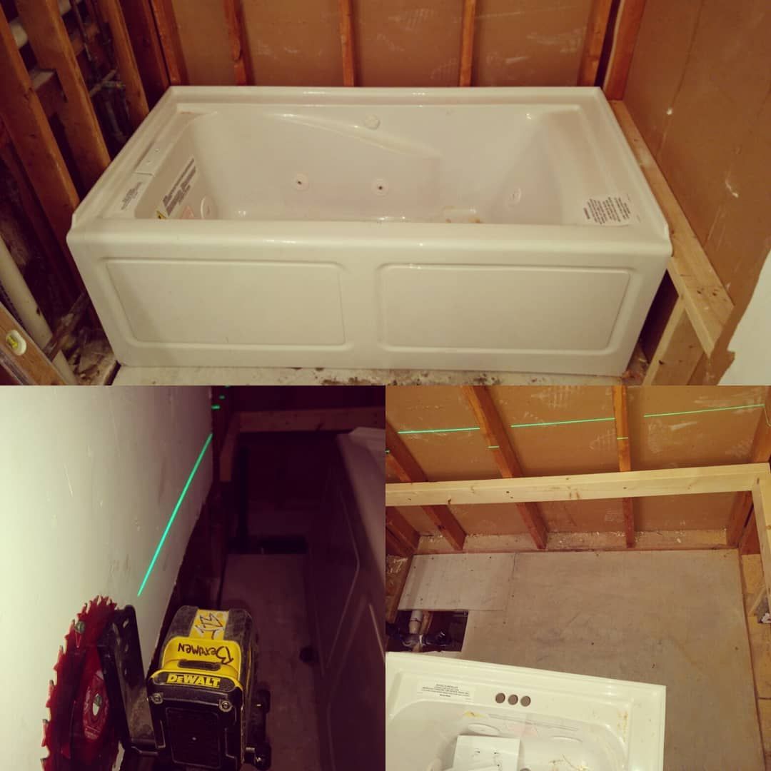 Installation of a white bathtub in a framed space, with a level and saw nearby.
