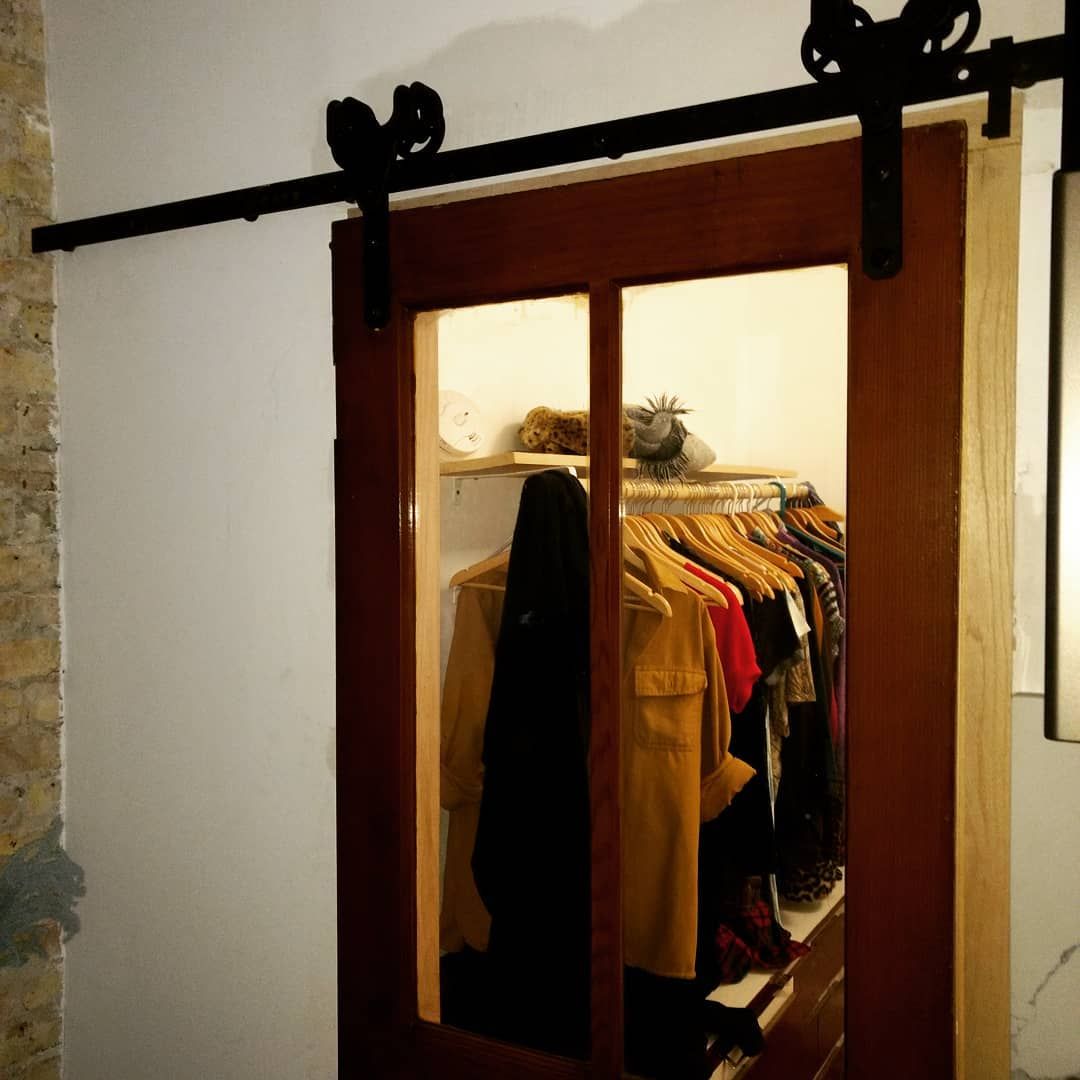 Barn door closet, dark brown frame with glass panel, sliding open to show clothes hanging on racks.