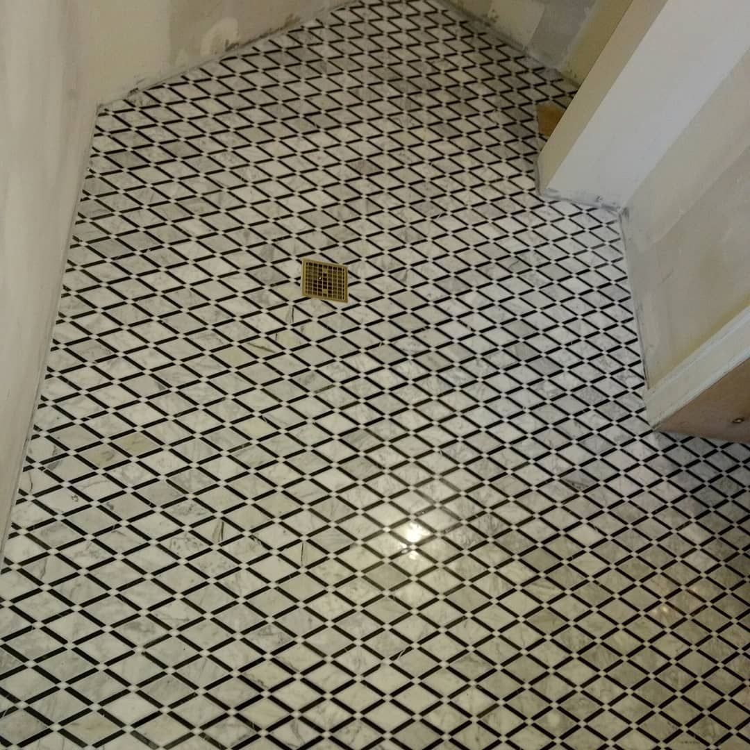 Shower floor with black and white diamond-patterned tile, centered drain, neutral walls.