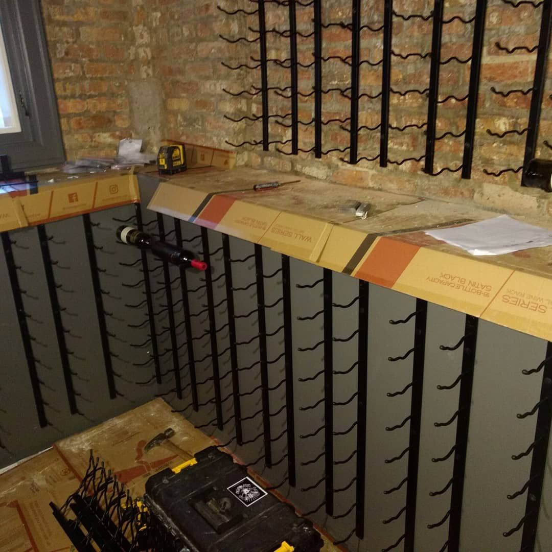 Wine cellar under construction, metal wine racks installed on gray walls, tools on wooden surfaces.