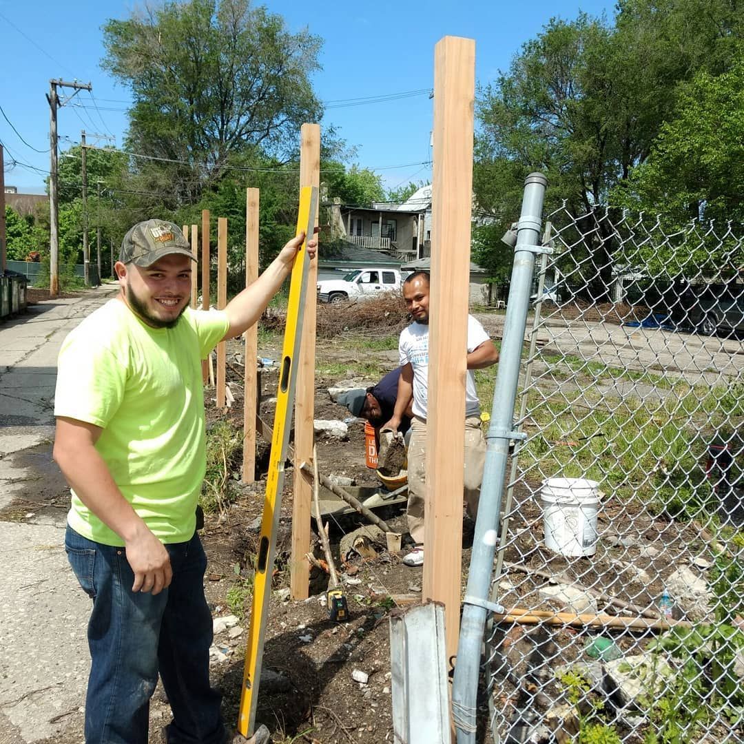Men installing a wooden fence outdoors on a sunny day. One man uses a level.