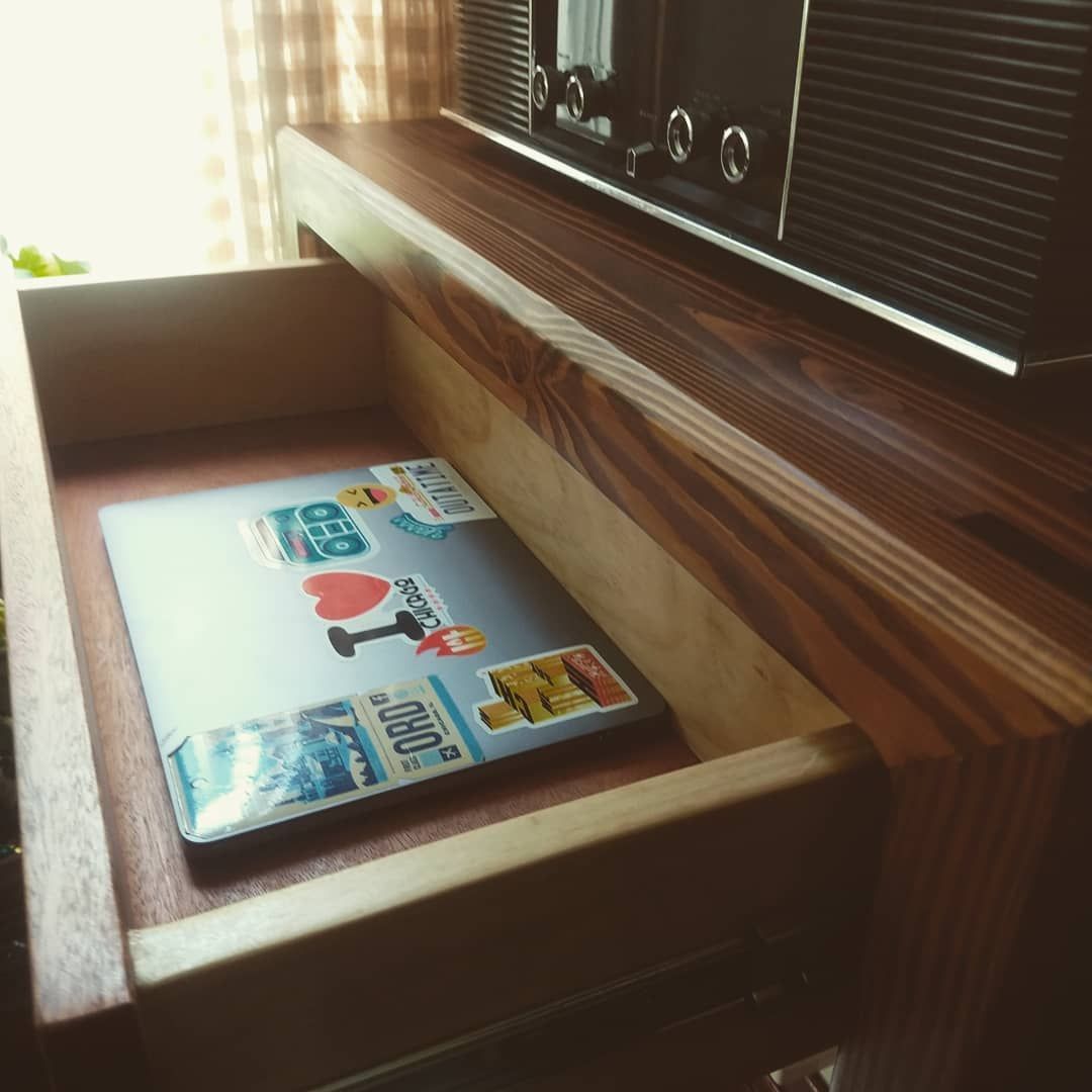 A laptop with stickers inside an open wooden drawer below a vintage radio.