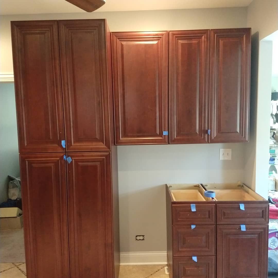 Brown kitchen cabinets installed against a light gray wall; lower cabinets not yet finished.