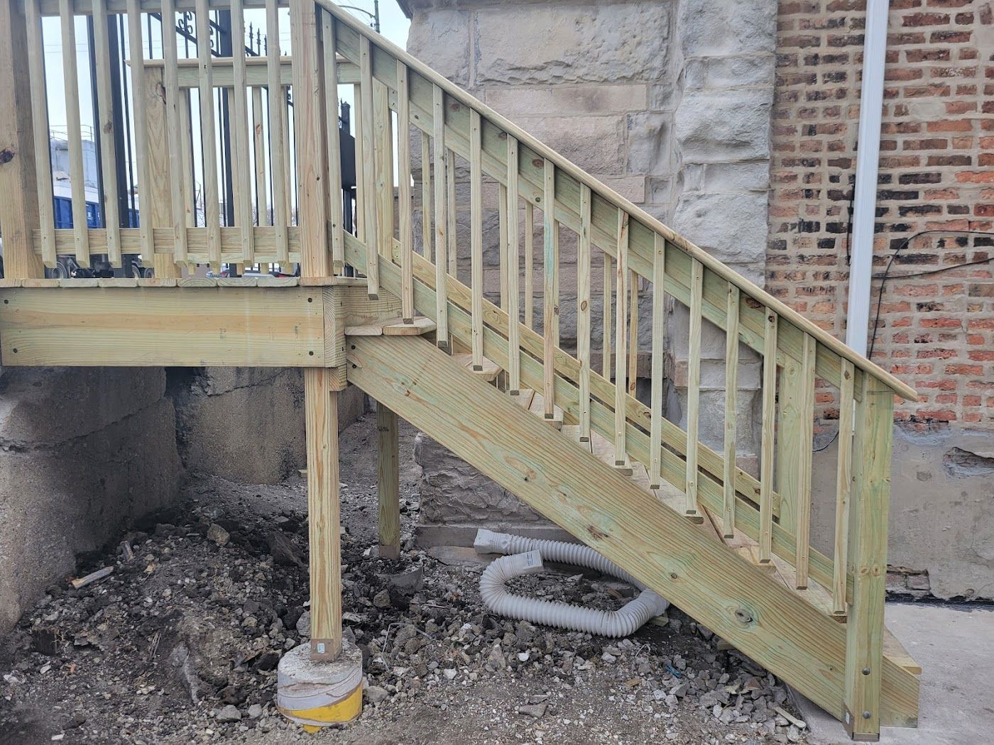 Wooden outdoor staircase leading up to a deck, set against a brick and stone wall.