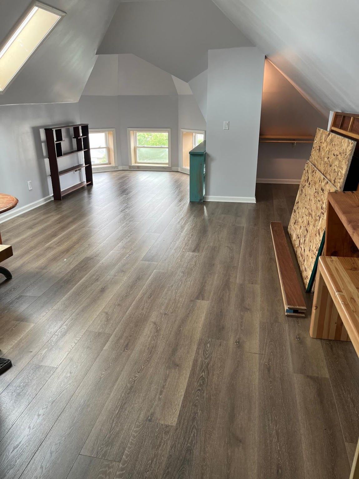 Spacious attic with angled walls, wood flooring, shelving, windows, and construction materials.