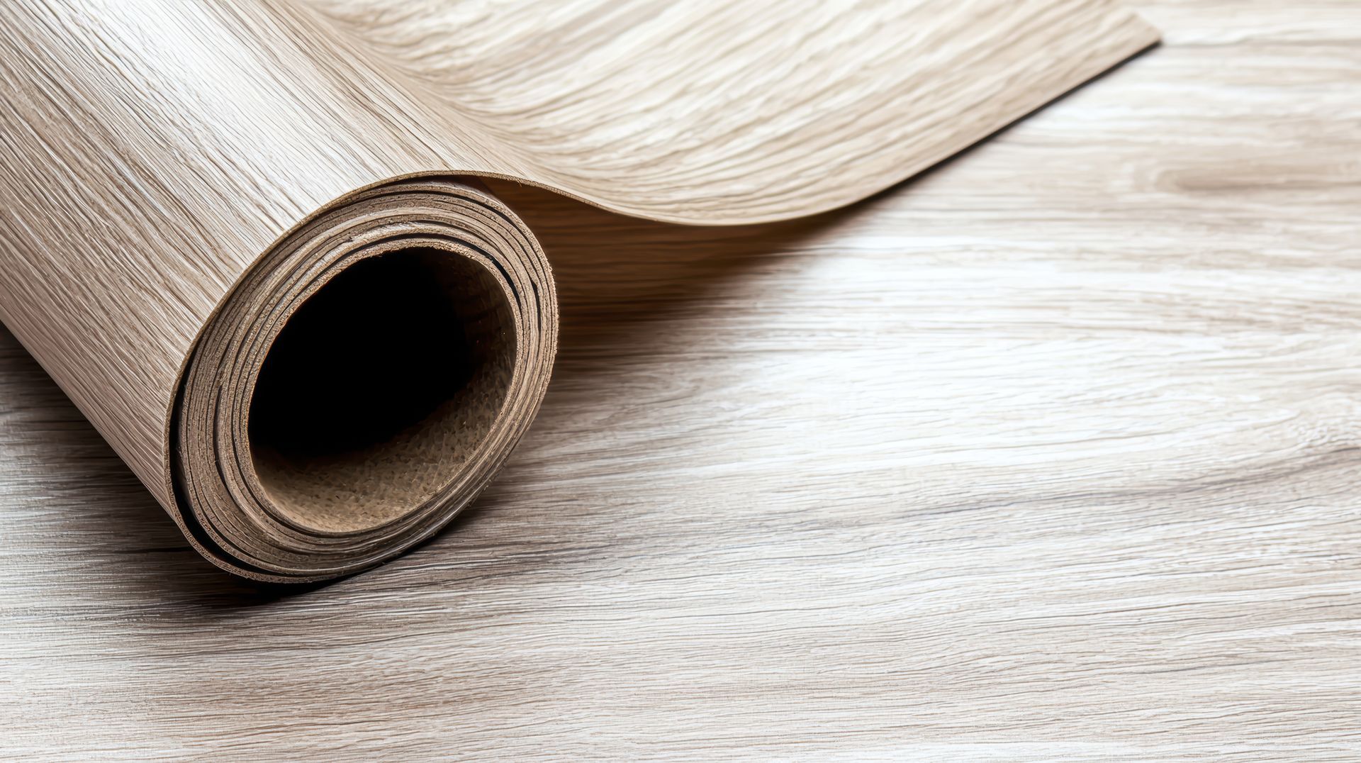 A roll of vinyl flooring is sitting on a wooden floor.