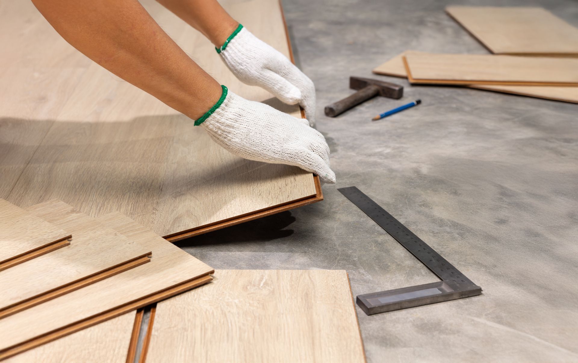 A person is laying wooden flooring on a concrete floor.