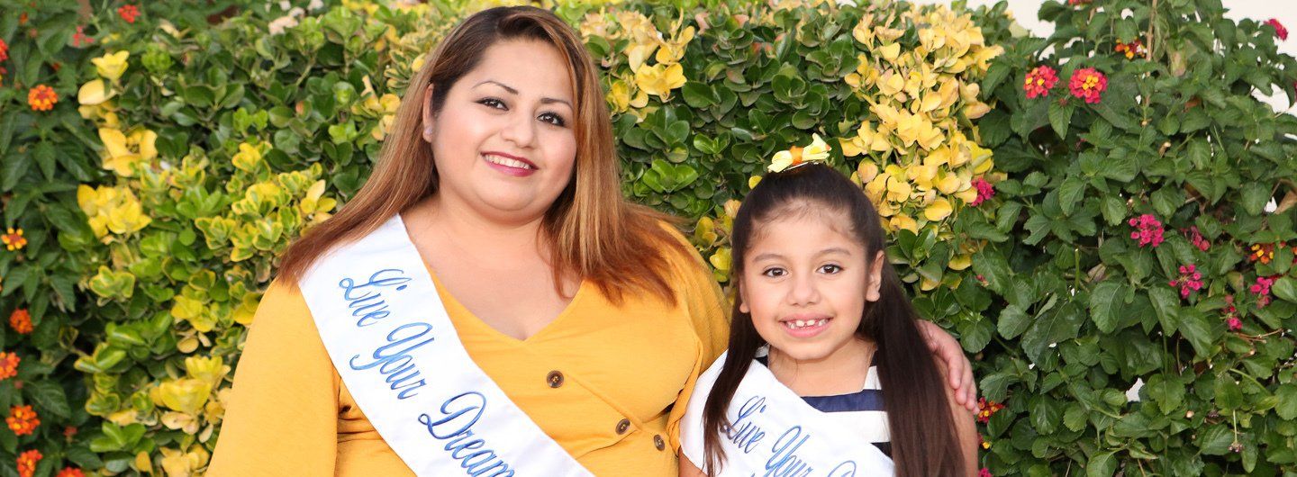 A woman and a little girl are posing for a picture in front of a bush who are part of the charity.