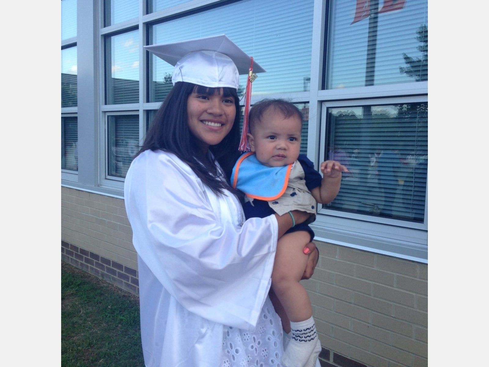 A woman in a graduation cap and gown is holding a baby