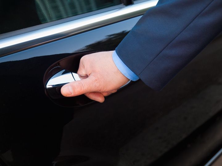 a man in a suit is opening the door of a black car