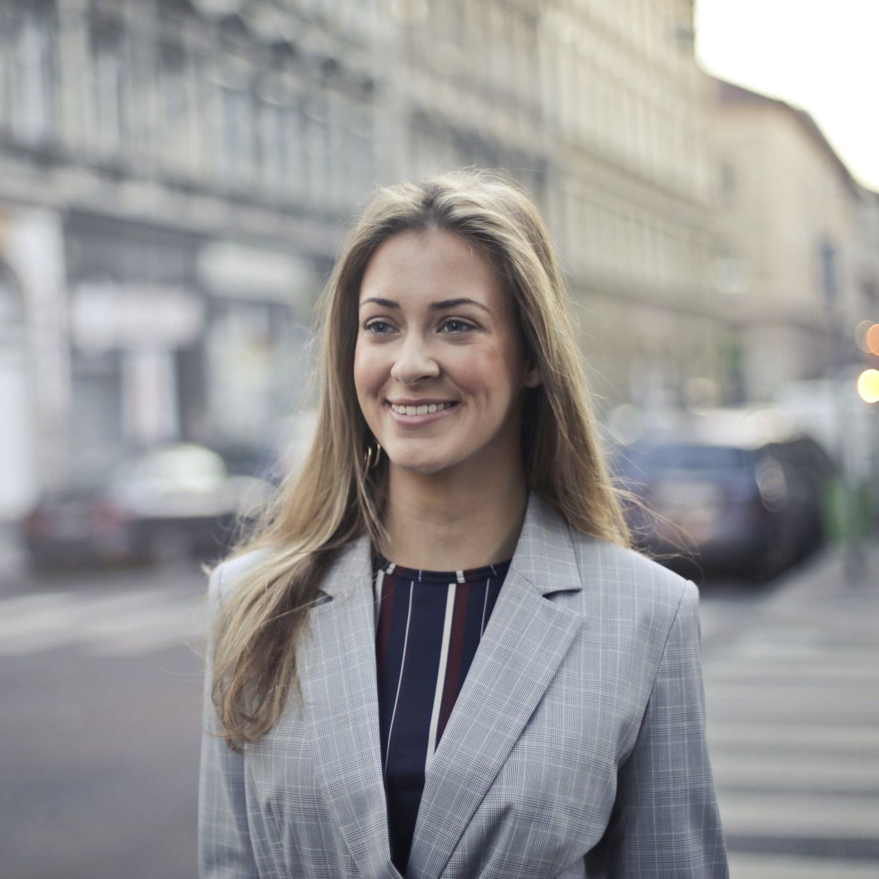 A woman in a suit is smiling while standing on a city street.