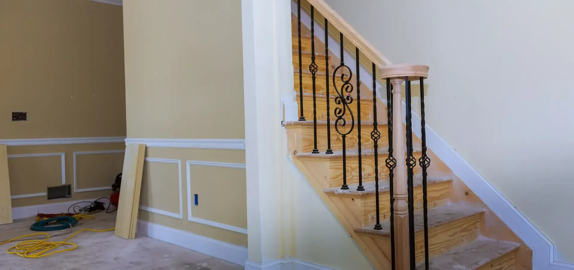 Staircase with wooden steps, black iron railing, and beige walls in a room under construction.