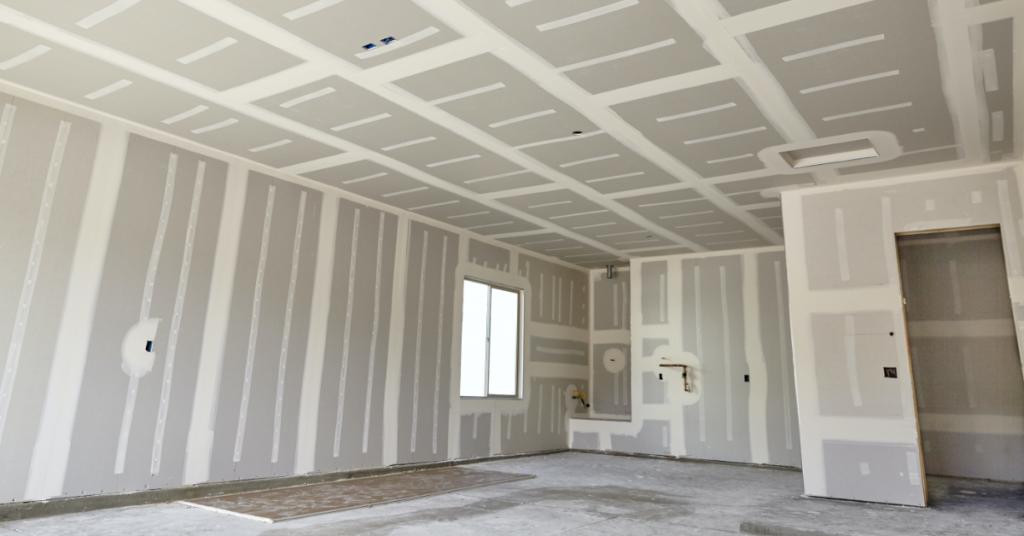 Interior of a room under construction, with drywall installed on walls and ceiling; bare concrete floor.