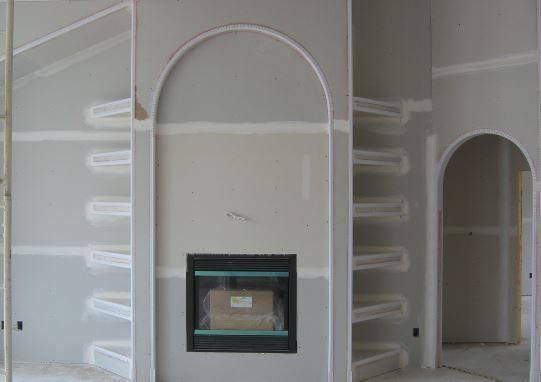 Drywall interior with arched openings and built-in shelving flanking a fireplace.