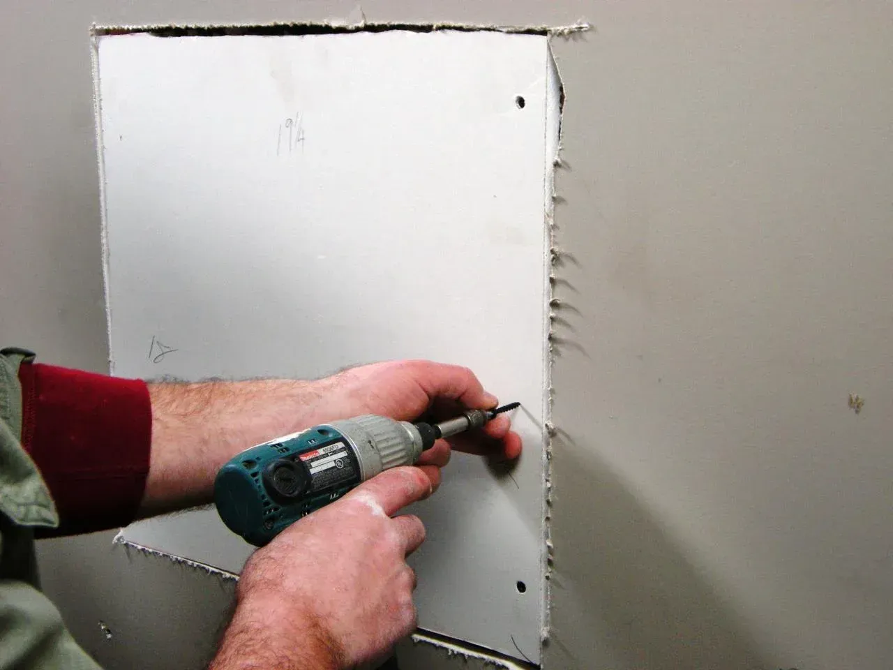Person using a drill to secure a drywall patch to a wall, patching a hole.