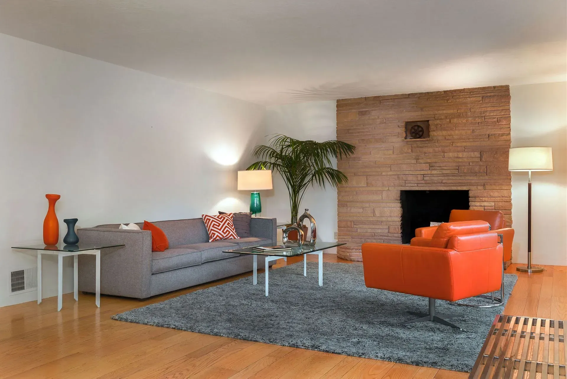 Living room with gray sofa, orange armchair, brick fireplace, and blue rug.