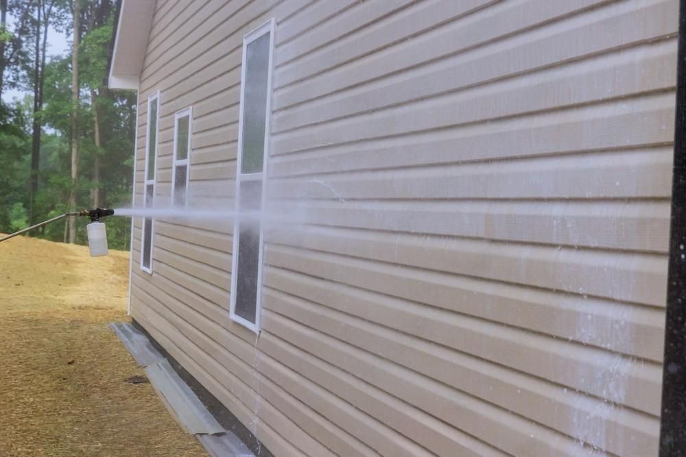 A person is cleaning the side of a house with a pressure washer.