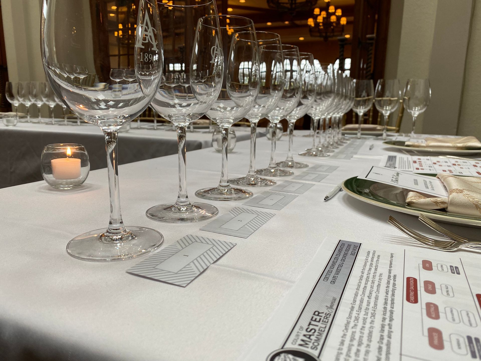 Wine glasses lined up on a table set for tasting, with accompanying cards and candles.