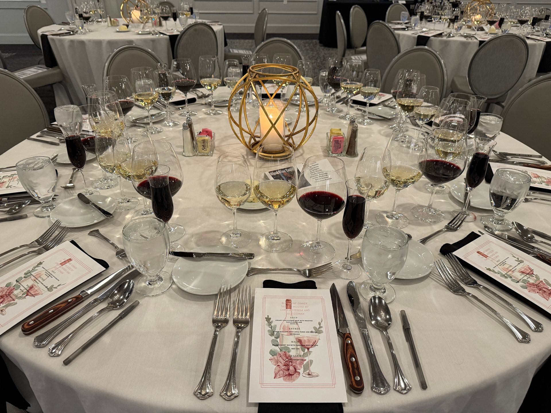 Formal dining table set with glassware, silverware, and menu; a centerpiece with a candle.