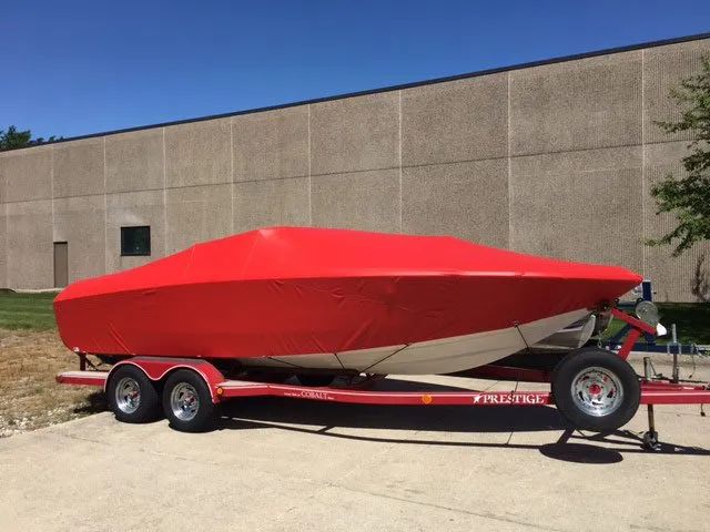 A red boat is on a trailer in front of a building.
