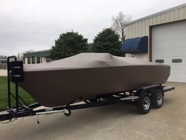 A boat with a cover on it is parked in front of a garage.