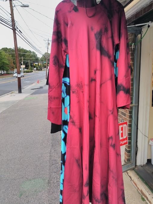 A long-sleeved, pink tie-dye dress with a black and blue floral side panel displayed on a mannequin outside a shop.