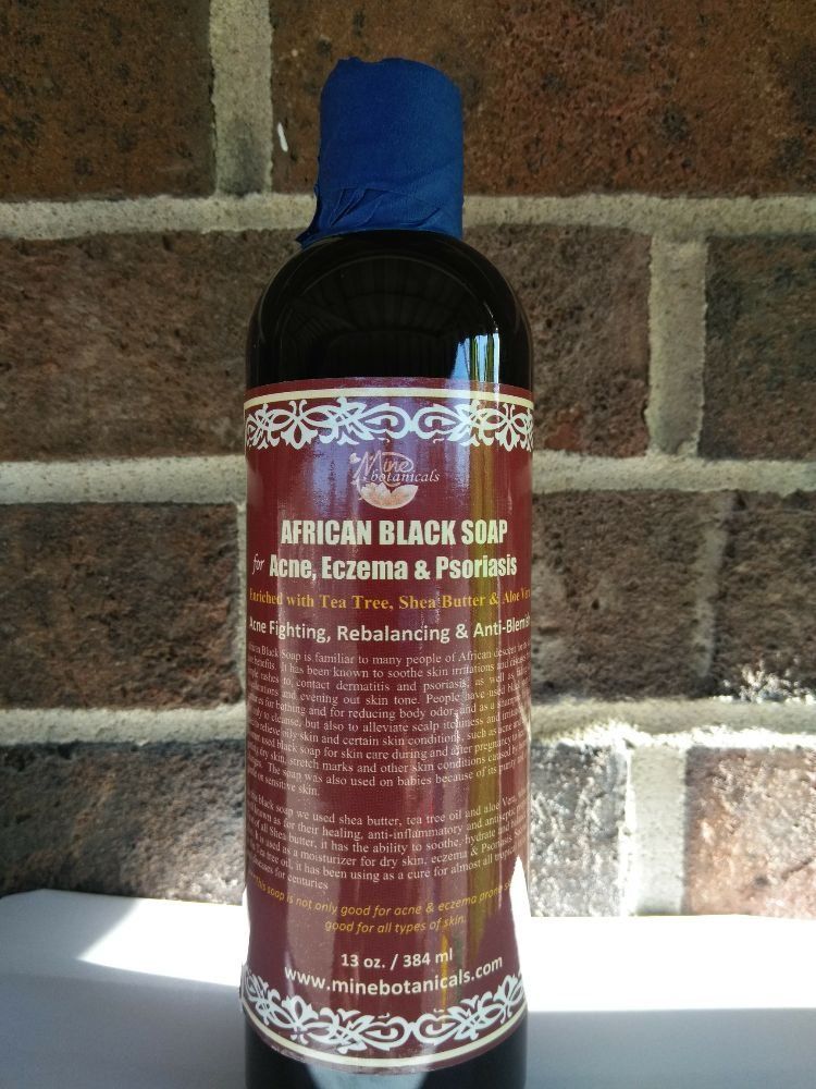 A bottle of African Black Soap for acne, eczema, and psoriasis, with a blue cap against a brick wall background.