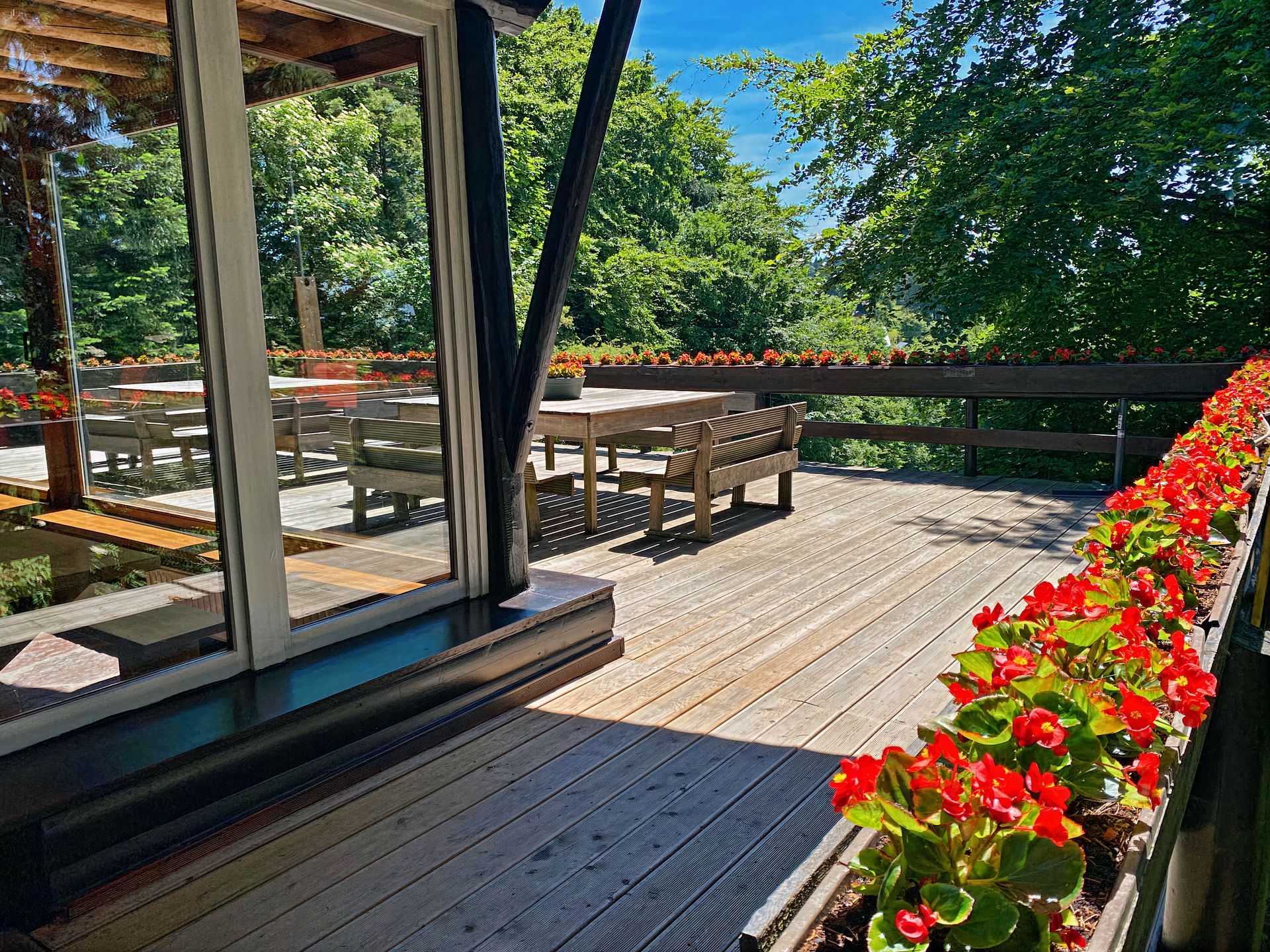 Une terrasse en bois avec des fleurs rouges et un banc.