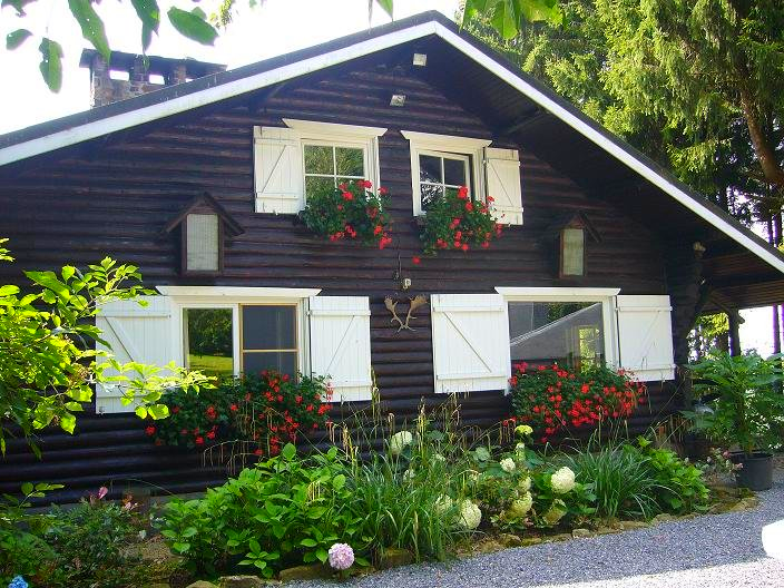 Een houten huis met witte luiken en bloemen op de ramen