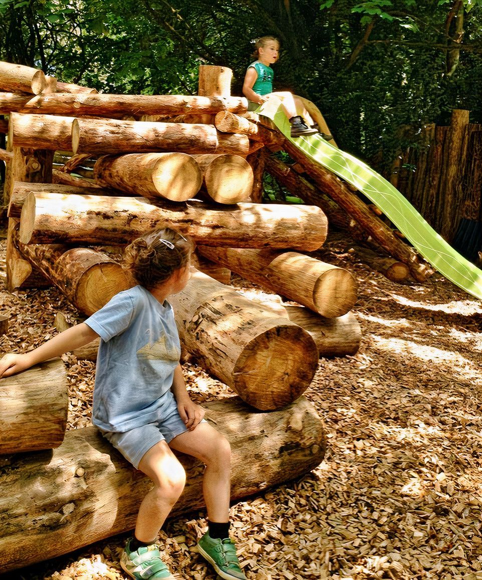 Un enfant est assis sur une bûche devant un toboggan.