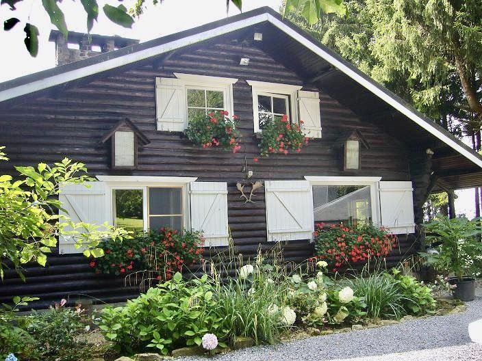 Une maison en bois avec des volets blancs et des fleurs aux fenêtres