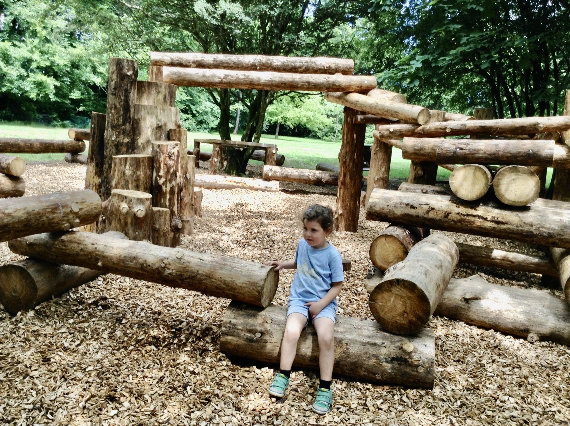 Een jonge jongen zit op een boomstam op een speelplaats.