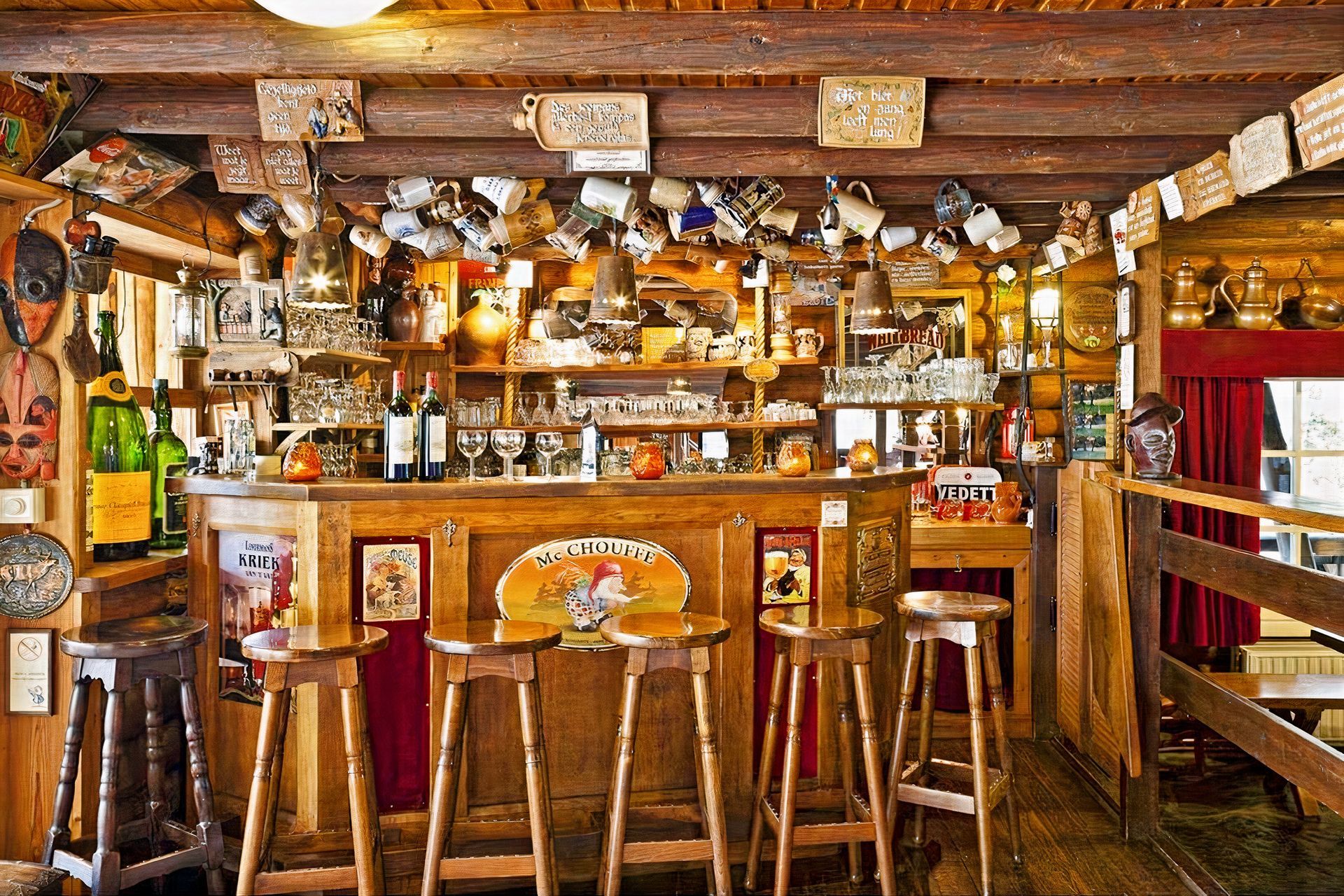 Un bar en bois avec des tabourets et des bouteilles suspendues au plafond.