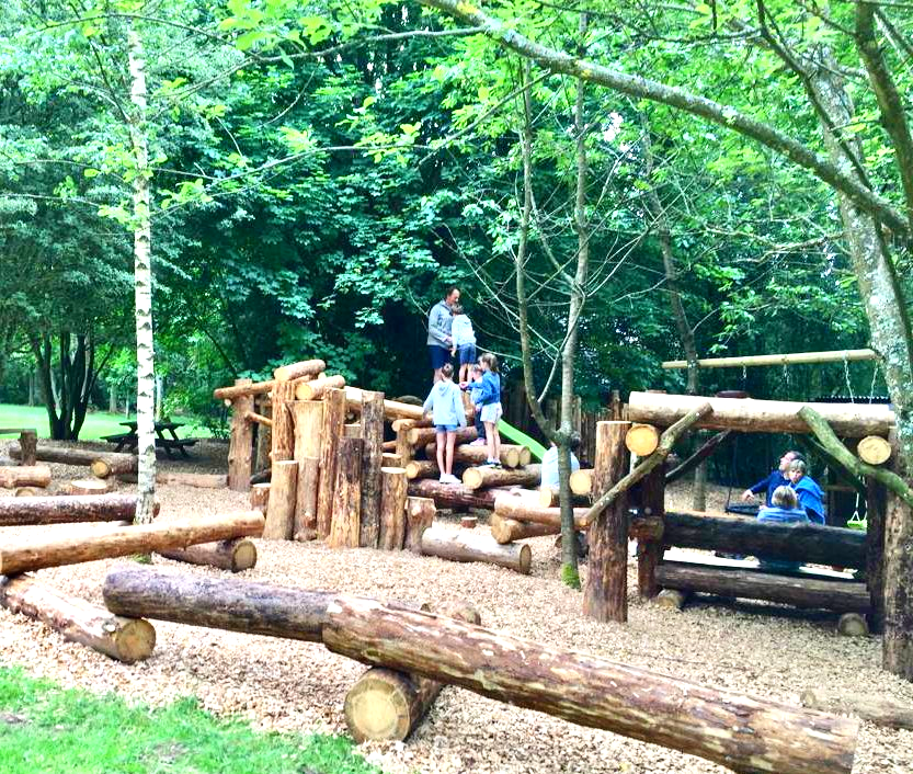 Een groep kinderen speelt op een houten speelplaats.