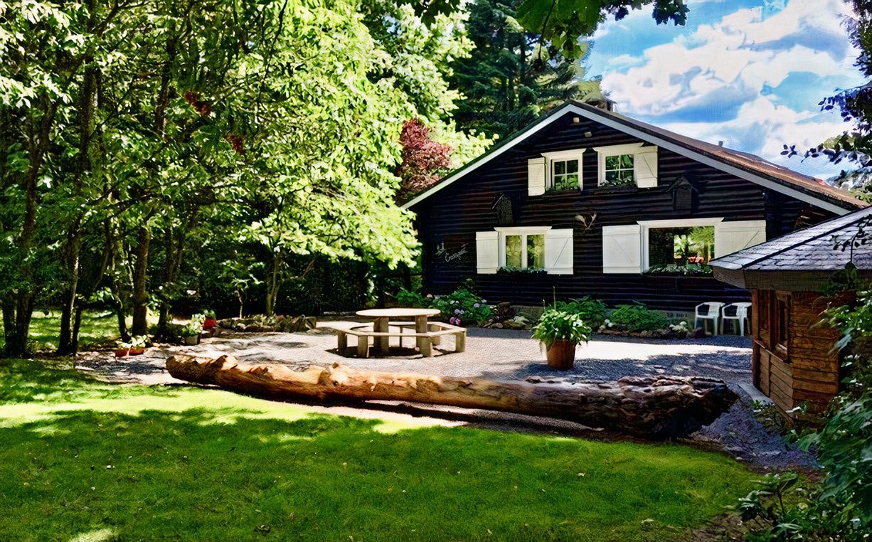Une cabane en rondins au milieu d'une forêt avec une table de pique-nique devant.