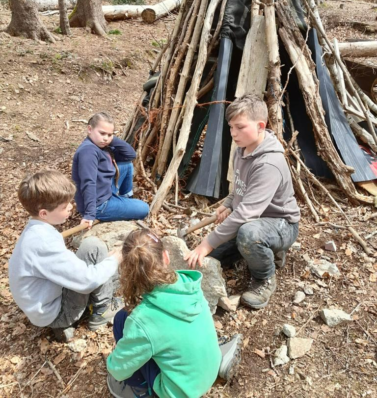 Een groep kinderen zit voor een houten constructie