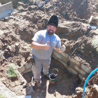 A man wearing a welding helmet is giving a thumbs up in the dirt.